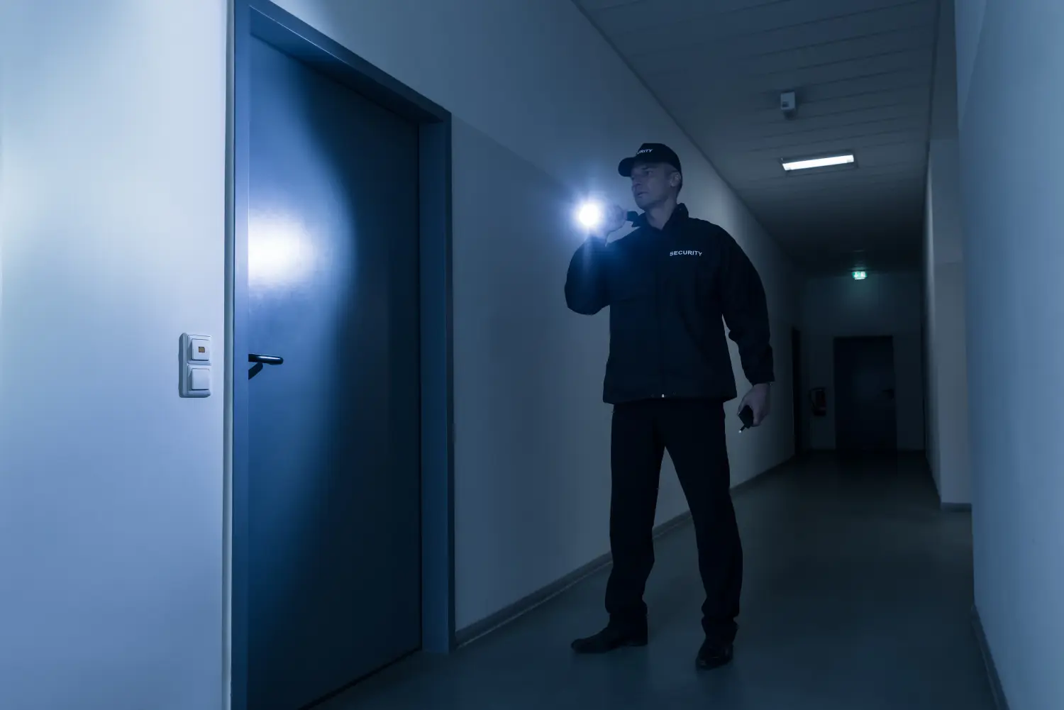 Sicherheitsbeamter mit Taschenlampe steht vor der Tür