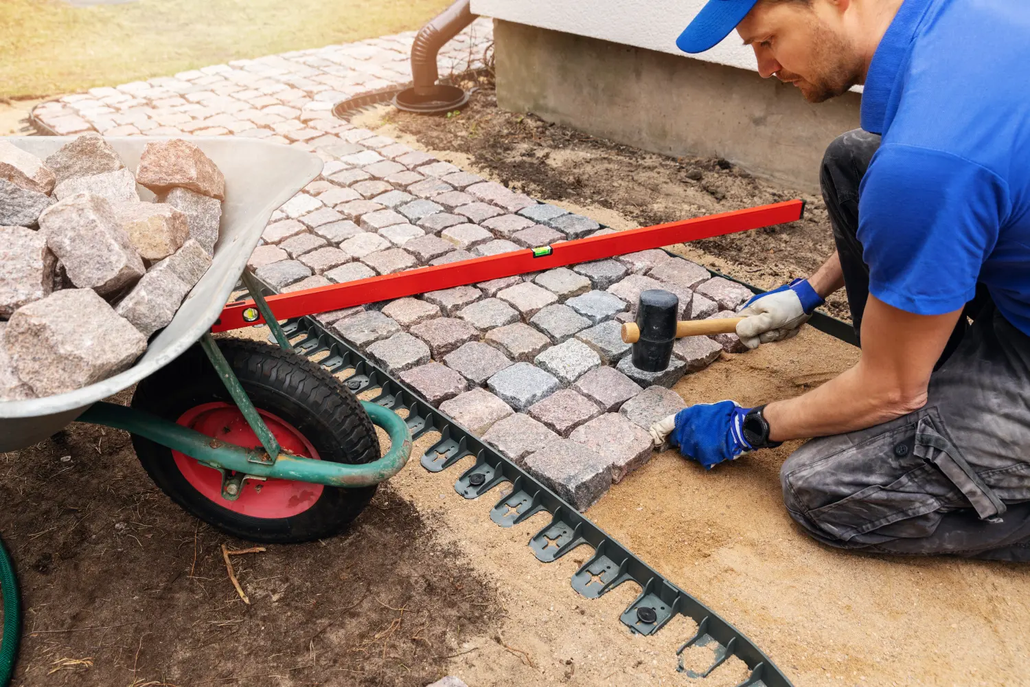 Arbeiter verlegt Granit-Kopfsteinpflasterweg rund um das Haus