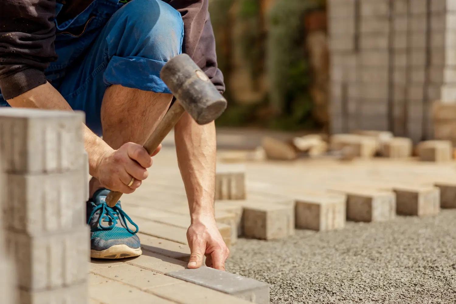 Junger Mann legt graue Betonpflasterplatten im Innenhof des Hauses auf Kiesfundament